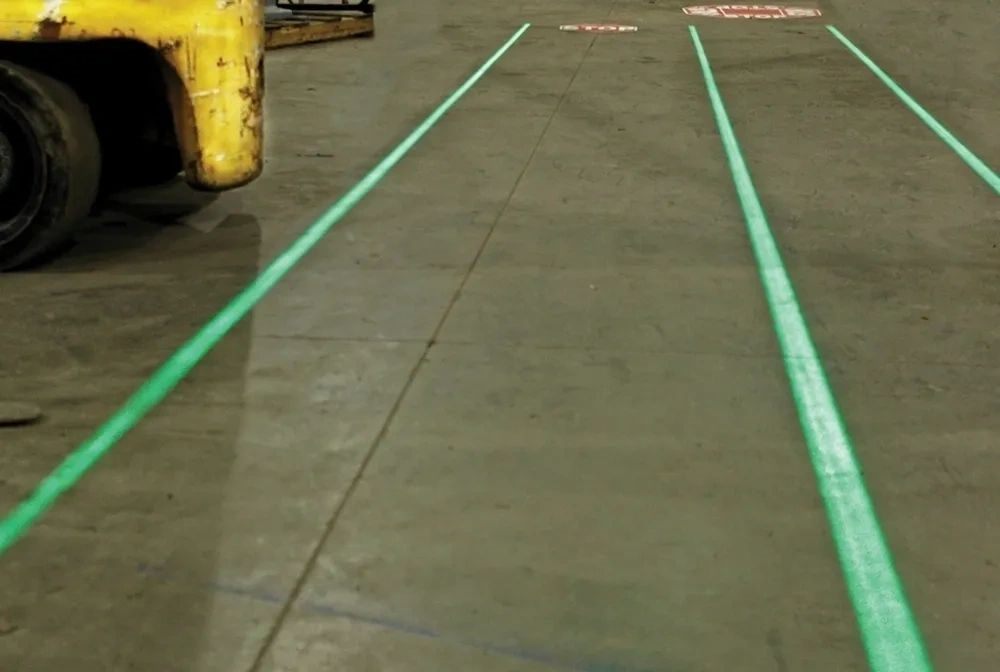 Projected green lane lines on a warehouse floor beside a forklift