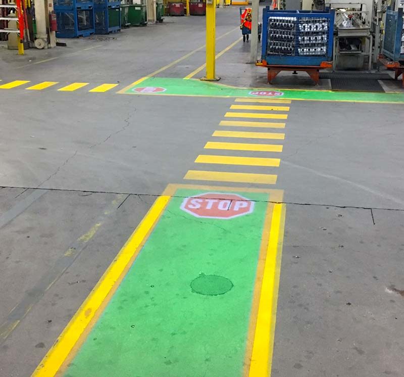 Projected green walkway and STOP signs at a forklift crossing in a plant